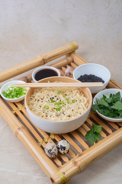 Plato de bambú blanco con fideos de huevo y platos con ingredientes en una bandeja de bambú sobre un fondo claro