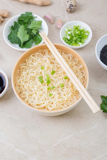 Plato de bambú blanco con fideos de huevo y platos con ingredientes sobre un fondo claro