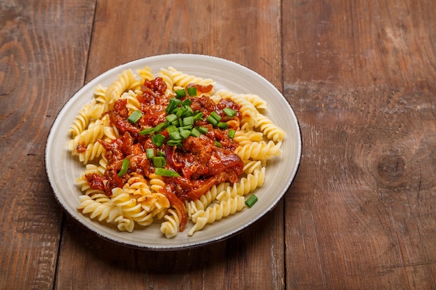 Plato beige con pasta boloñesa sobre una mesa de madera espolvoreada con cebollas verdes