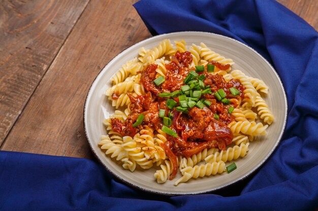 Plato beige con pasta boloñesa sobre una mesa de madera sobre una servilleta azul