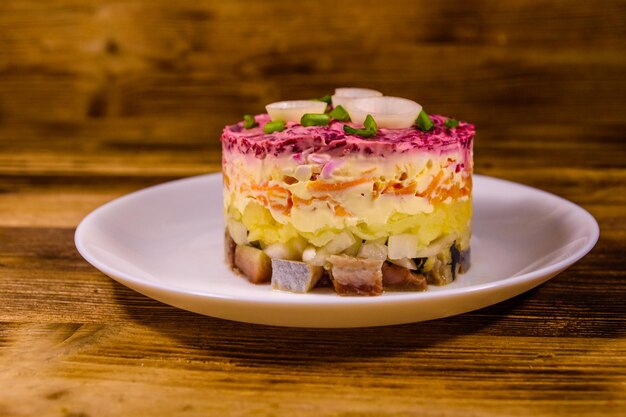 Plato blanco con arenque de ensalada de año nuevo tradicional ruso bajo abrigo de piel en una mesa de madera rústica