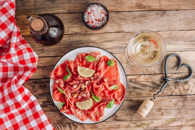 Plato blanco con carpaccio de ternera con rúcula lima y vino blanco sobre fondo rústico de madera Vista superior