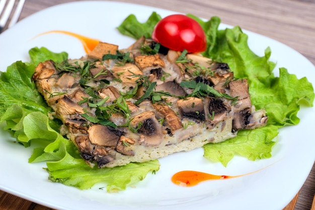 Un plato blanco con champiñones gratinados y verduras.