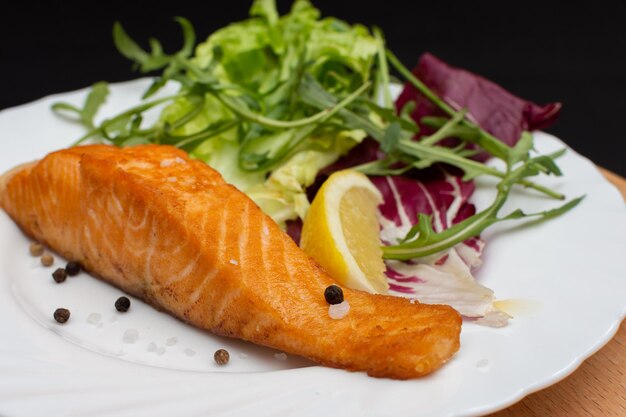 Un plato blanco cubierto con un trozo de salmón y una ensalada fresca