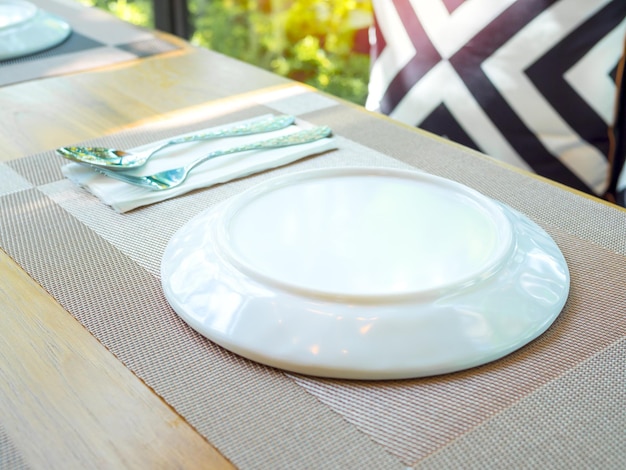 Plato blanco con cuchara y tenedor en el tapete de la mesa de madera