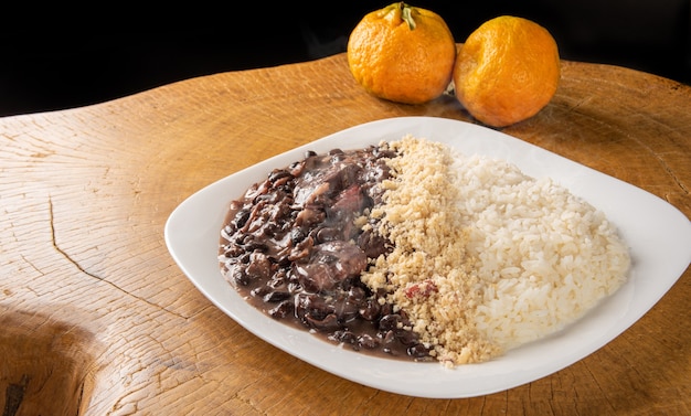 Plato blanco con una deliciosa feijoada brasileña, arroz y farofa, con dos naranjas sobre madera rústica