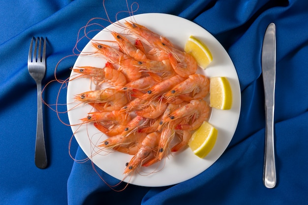 Plato blanco con deliciosos camarones con limón servido en azul con tenedor y cuchillo. Vista superior