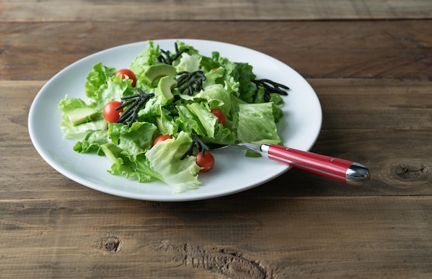 Plato blanco de ensalada mixta con algas tomates lechuga y aguacate Fondo de madera Espacio de copia