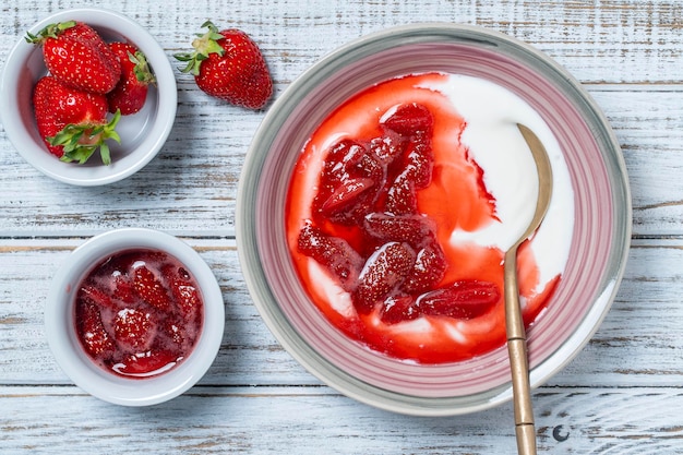 Plato blanco con fresas rojas y yogur natural en una mesa de madera vista superior