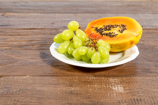 Plato blanco con frutas: papaya y uva, sobre una mesa de madera rústica