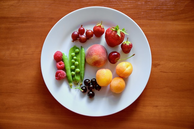 En un plato blanco grande hay diferentes frutas y bayas