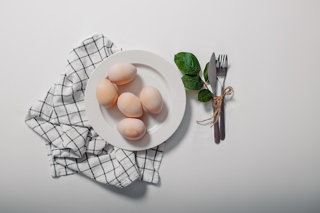 Plato blanco con huevos sobre fondo blanco Tarjeta de Pascua feliz con plato con huevos y hojas verdes
