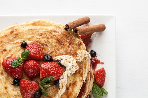 Plato blanco lleno de panqueques con frambuesas, fresas, arándanos y miel.