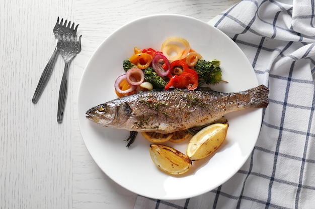 Plato blanco con pescado al horno y guarnición en la mesa