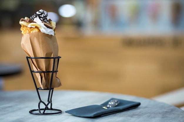 Plato blanco con postre helado en taza de oblea con galletas de chocolate y decoración creativa sobre fondo interior colorido borroso.