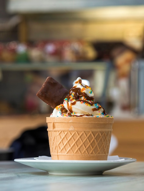 Plato blanco con postre helado en taza de oblea con galletas de chocolate y decoración creativa en la superficie interior colorida borrosa