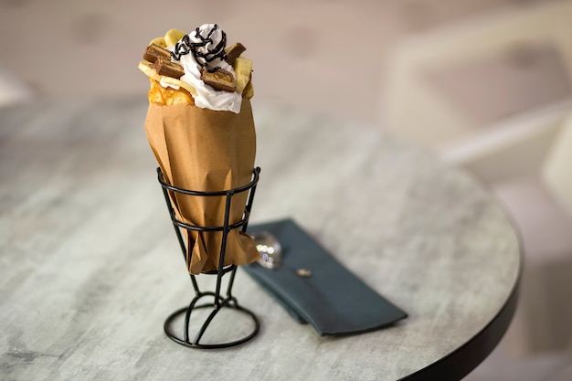 Foto plato blanco con postre de helado en taza de oblea con galletas de chocolate y decoración creativa topping sobre fondo interior colorido borroso.