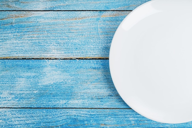 Un plato blanco redondo vacío sobre una mesa de madera azul.