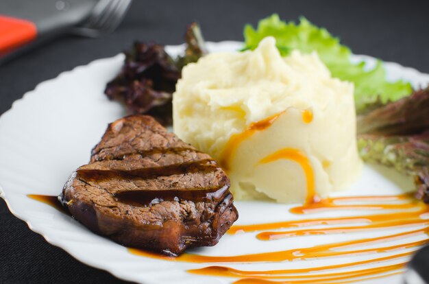 En un plato blanco, sobre una hermosa tela y fondo oscuro puré de papas con carne de res en salsa balsámica bellamente pulida