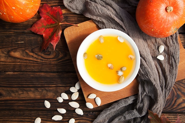 Plato blanco de sopa de calabaza y hoja de arce sobre fondo oscuro de madera rústica