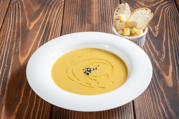 Plato blanco de sopa de crema con picatostes en mesa de madera