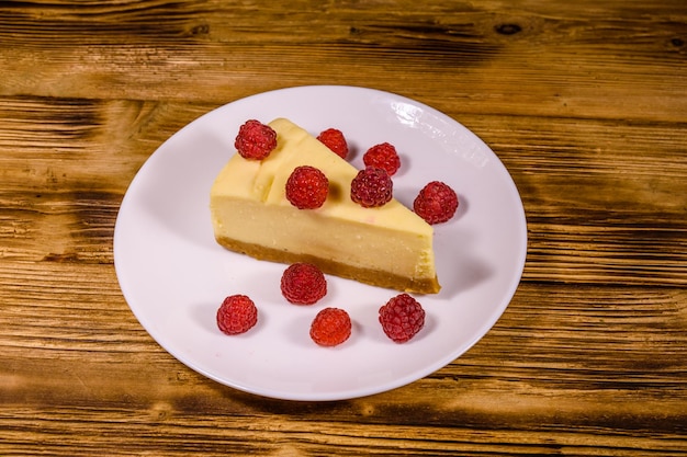 Plato blanco con tarta de queso Nueva York y frambuesas sobre mesa de madera rústica