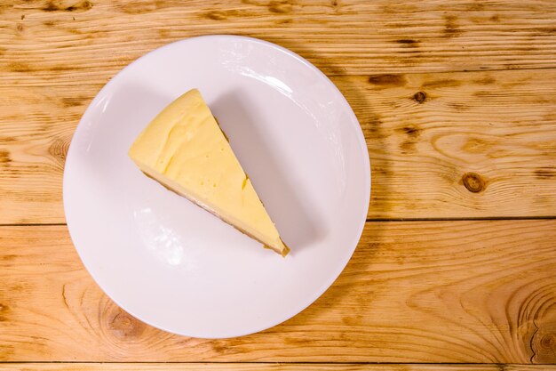 Plato blanco con tarta de queso Nueva York sobre mesa rústica de madera. Vista superior