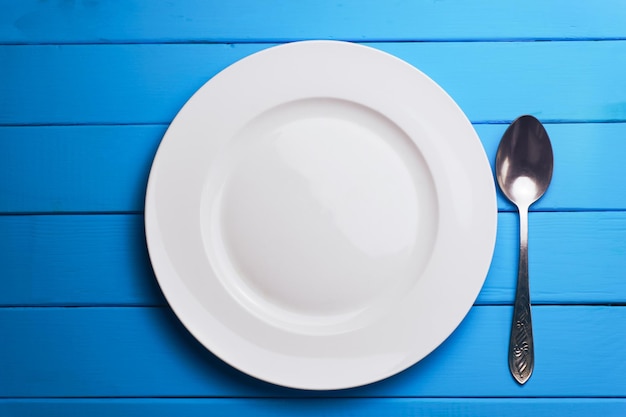 Foto plato blanco y un tenedor con una cuchara en un fondo de mesa de madera azul