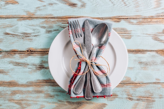 Plato blanco vacío con cubiertos y servilleta en la mesa de madera rústica.