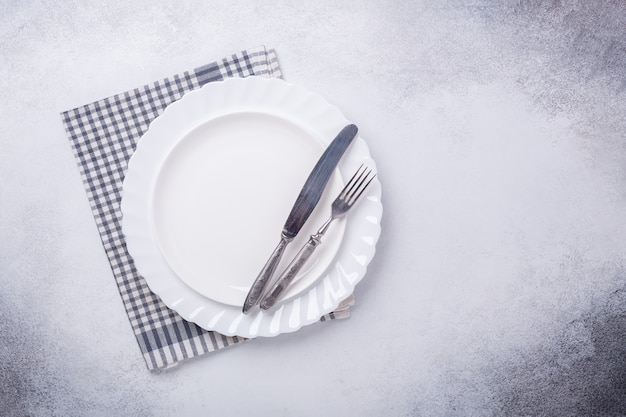 Plato blanco vacío, servilleta de lino, cuchillo y tenedor sobre fondo de piedra