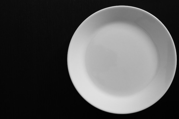 Plato blanco vacío sobre mesa de madera negra. Cerca de utensilios de cocina