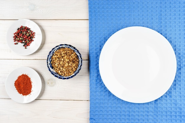 Plato blanco vacío sobre una servilleta azul sobre una mesa de madera con un conjunto de especias alrededor de la vista superior