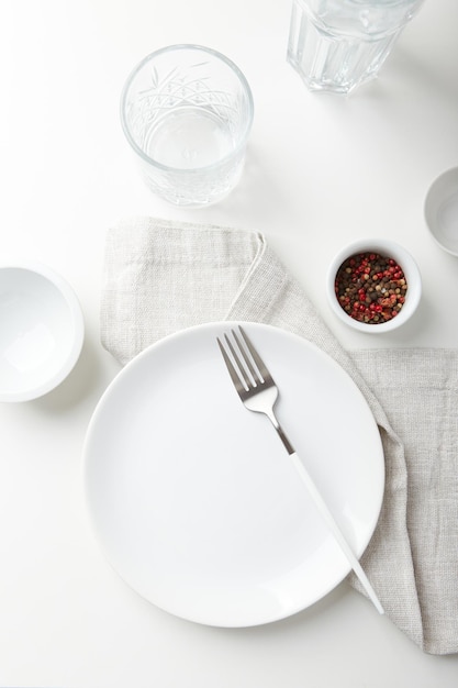 Plato blanco vacío con un tenedor y tazones pequeños sobre un fondo claro