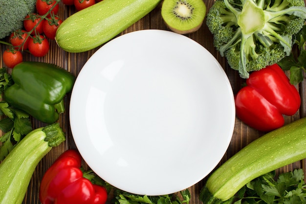 Plato blanco vacío, verduras y frutas en el fondo marrón. Ingredientes alimentarios saludables. Vista superior. Copie el espacio.