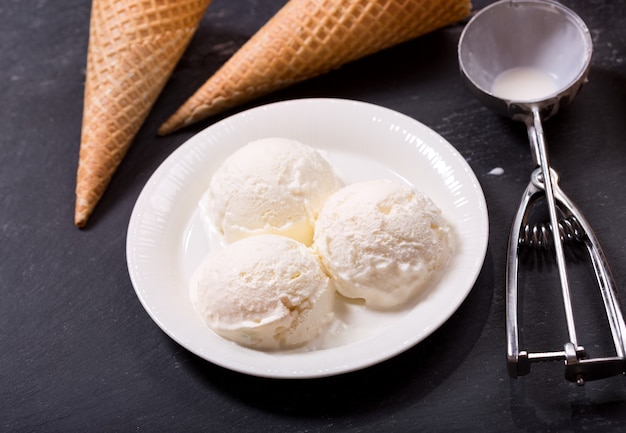 Foto plato de bolas de helado y conos de galleta sobre fondo oscuro