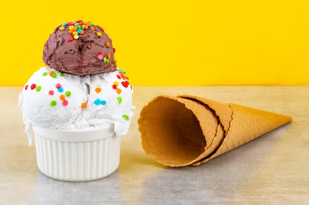 Plato de bolas de helado de vainilla y chocolate con chispitas de trozos de chocolate y conos de galleta en amarillo.