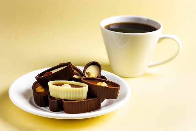 Un plato con bombones y una taza de café sobre un fondo amarillo