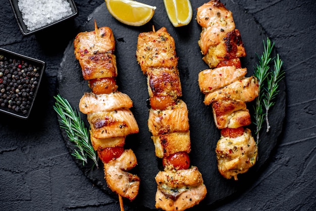 Foto un plato de brochetas de pollo con rodajas de limón y limones sobre un fondo oscuro.