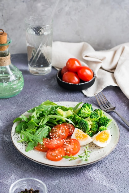 Un plato con brócoli, rúcula, tomate y huevo cocido en un plato sobre la mesa Vista vertical