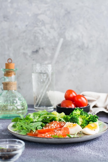 Un plato con brócoli tomate rúcula huevo cocido y semillas de sésamo en un plato Vista vertical