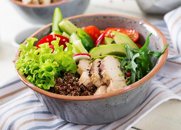 Plato Buda con filete de pollo, quinua, aguacate, pimiento dulce, tomate, pepino, rábano, ensalada de lechuga fresca y sésamo. Concepto de tazón de desayuno de desintoxicación y superalimentos saludables.