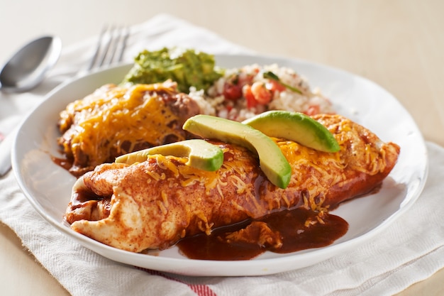 Foto plato de burrito mexicano con salsa de enchilada roja, frijoles fritos, arroz y guacamole