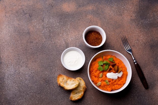 Plato de calabaza con rodajas de baguette tostado, especias y crema agria sobre un fondo marrón.