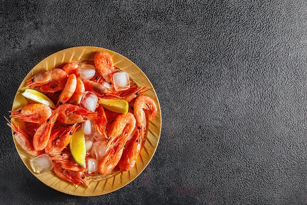 Plato con camarones crudos, marisco y hielo, con rodajas de lima sobre un fondo oscuro, plano