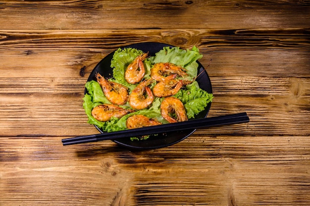 Plato con camarones a la parrilla, hojas de lechuga y palillos en una mesa de madera