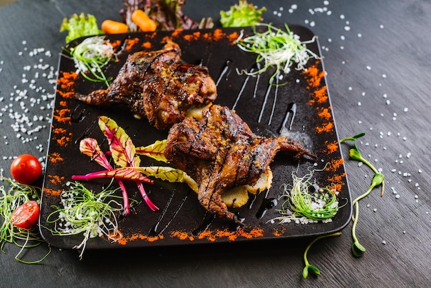 Un plato con carne de codorniz asada con verduras sobre fondo negro