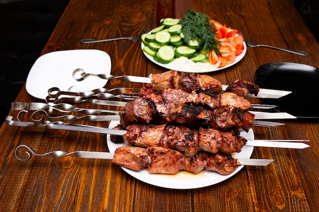 Un plato con carne de kebab grill barbacoa frita al fuego, ensartada en palos de metal, junto a un plato con verduras para el plato listo.