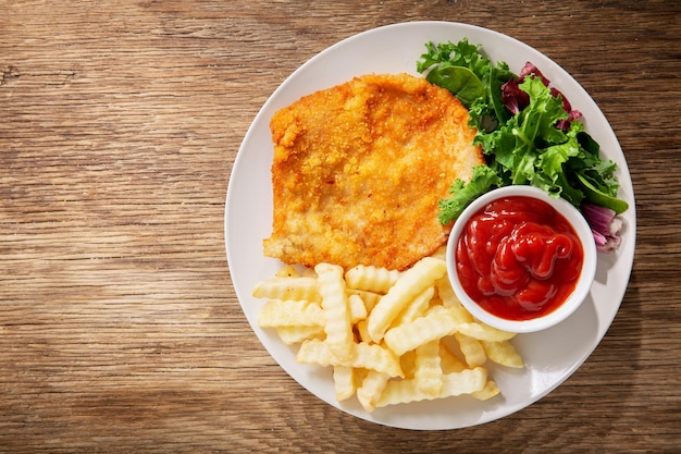 Plato de carne de pollo empanada frita o Schnitzel con papas fritas y ensalada