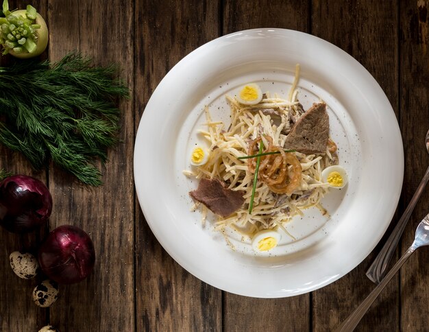 Un plato de carne y queso, decorado con huevos de codorniz y cebolla sobre tablas de madera, vista superior