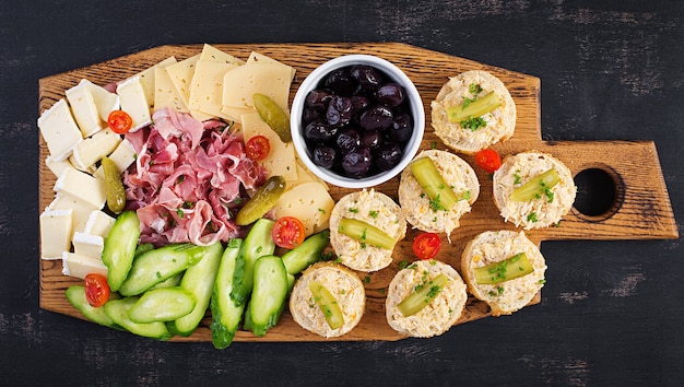 Plato de catering de antipasto con jamón, queso, canapé y aceitunas negras sobre una tabla de madera. Vista superior, arriba